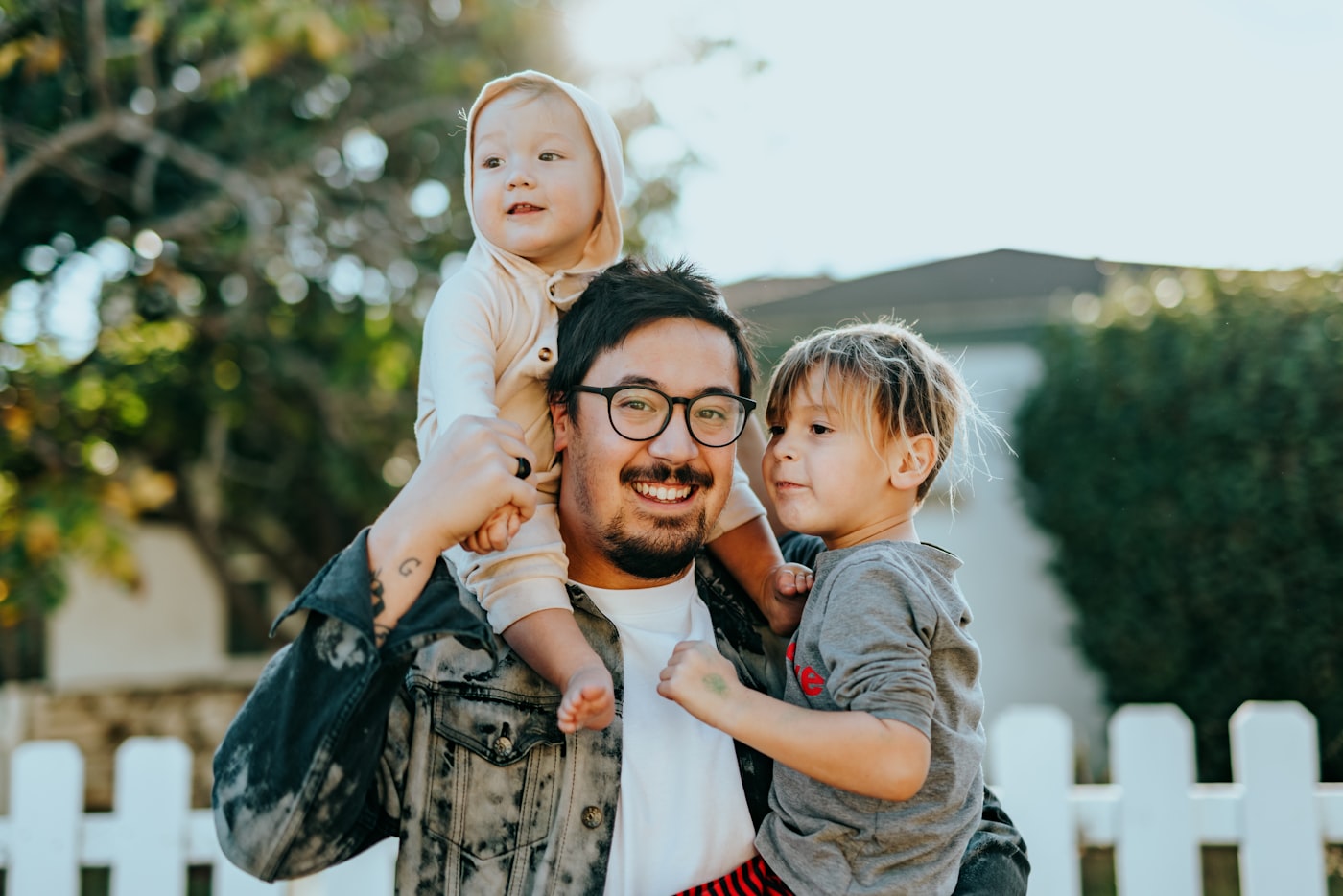 Pai sorrindo com os filhos em frente à casa nova